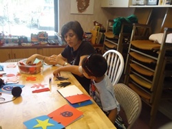 Photo of a counselor and child making a scrap book with hand prints, ornaments, yarn, and stars