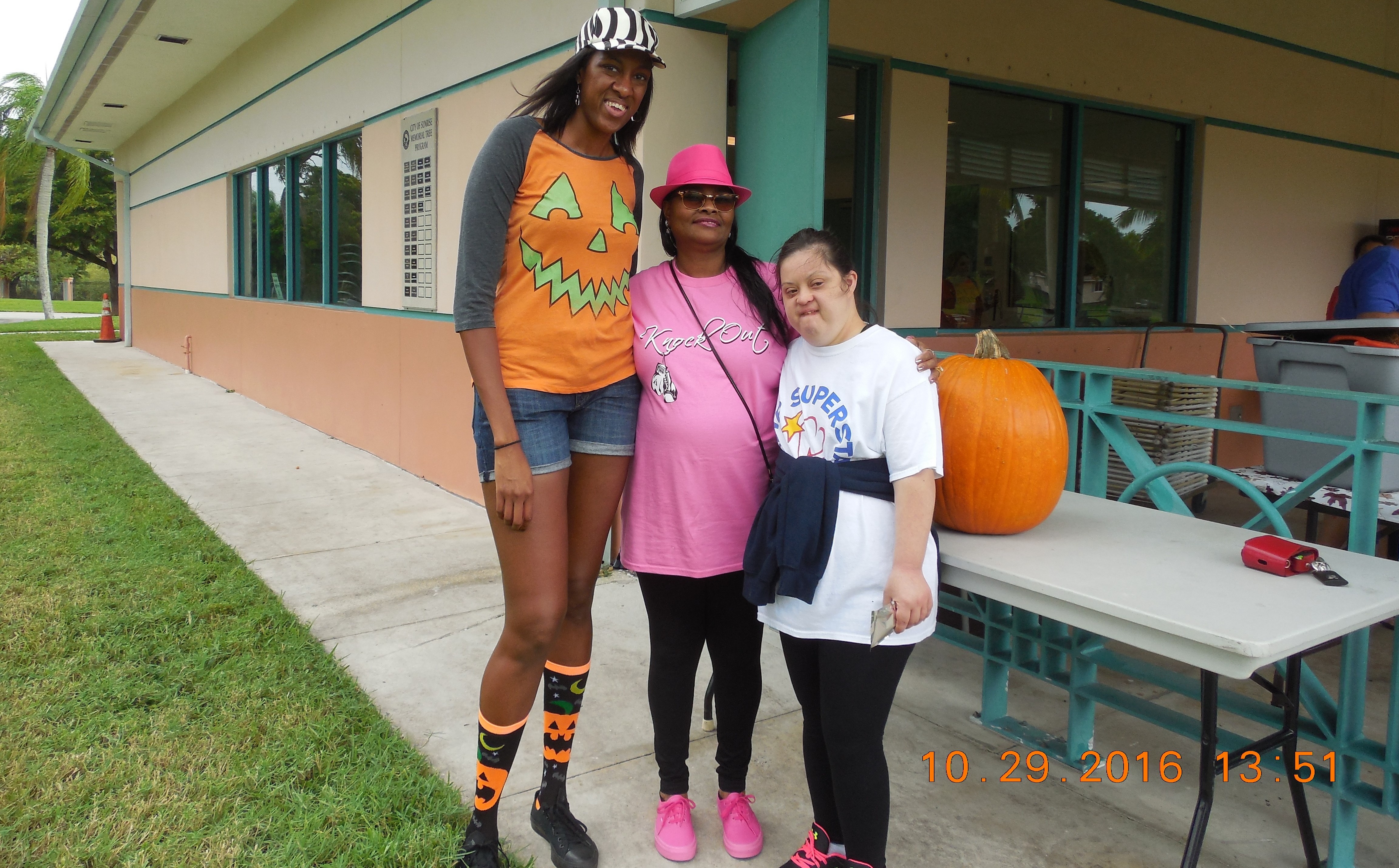 Three women of various ages stand next to a pumpkin