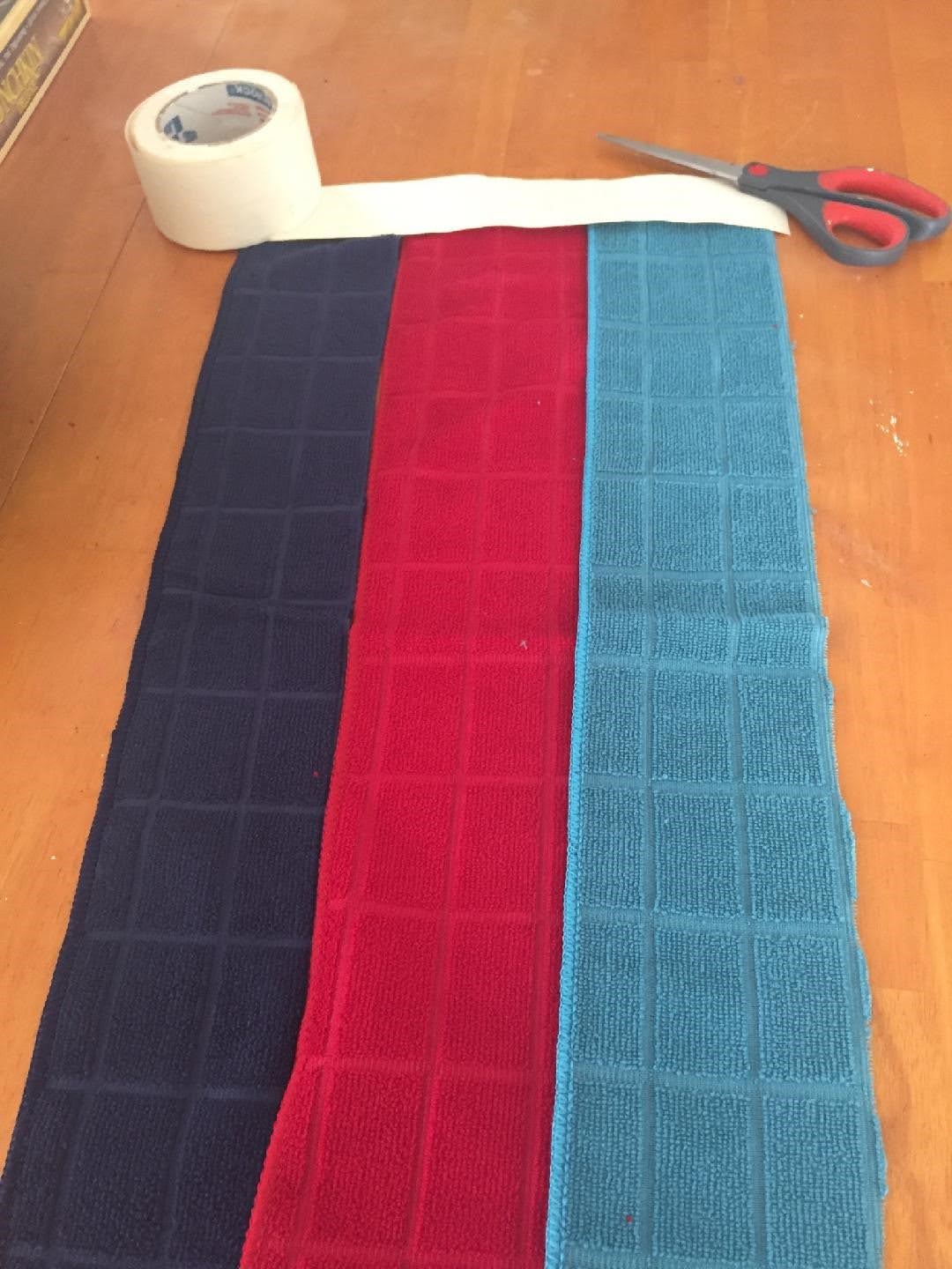 Three strips of towel laying side by side on table. Each is a different color.